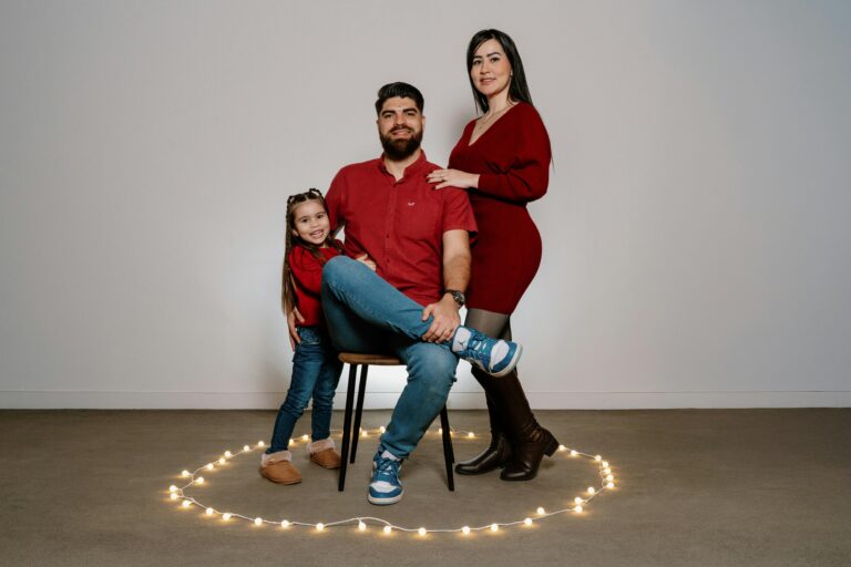 Family portrait featuring a couple with their daughter surrounded by decorative lights indoors.